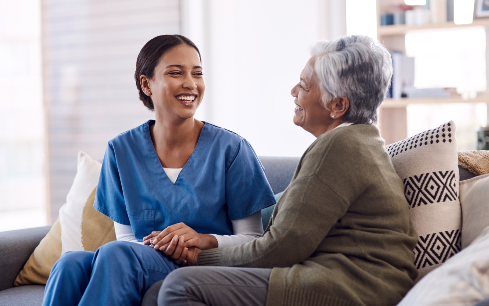 A caregiver and senior woman talking together on a sofa at home